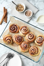 Tasty cinnamon rolls in baking dish served on white marble table, flat lay
