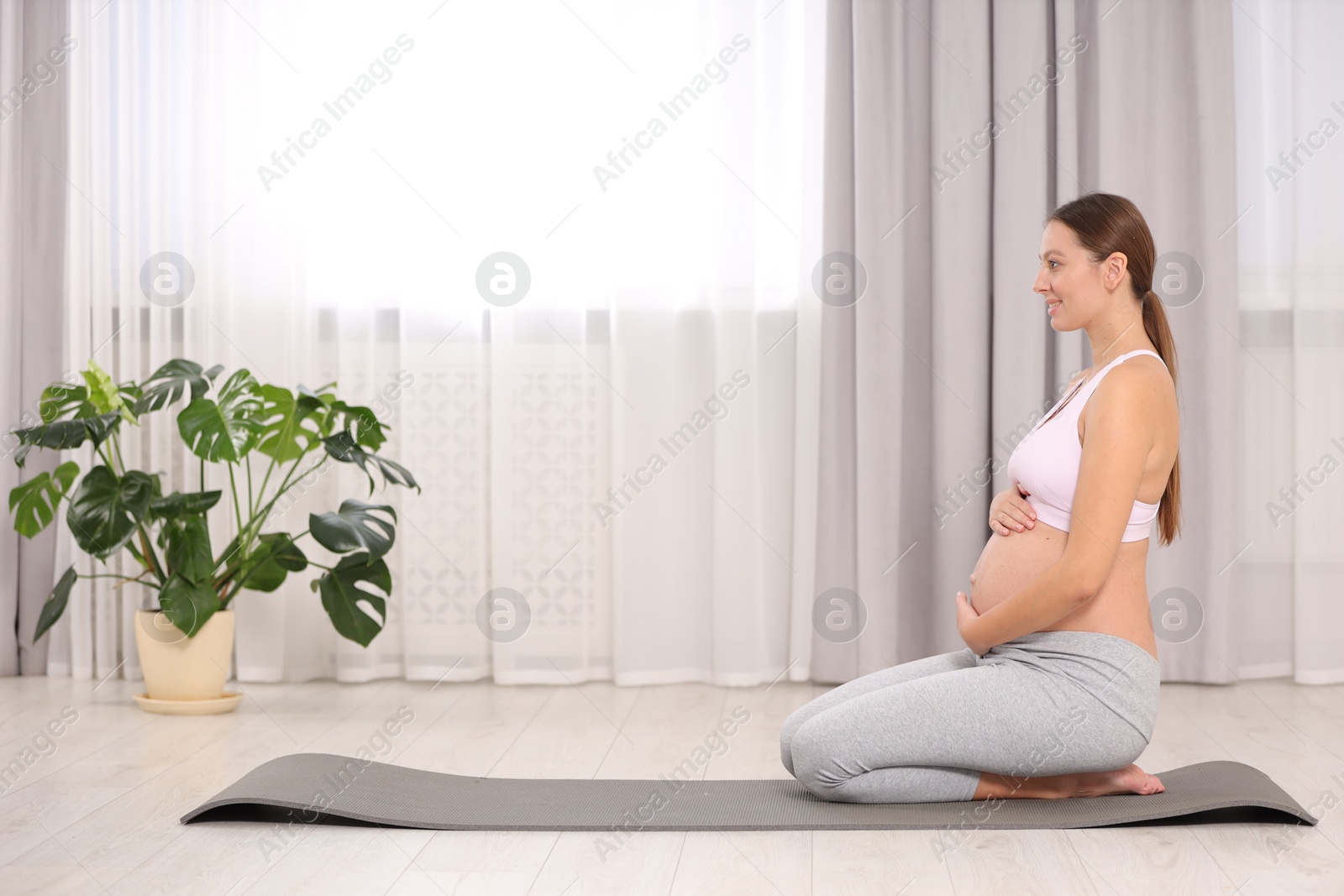 Photo of Pregnant woman sitting on yoga mat at home