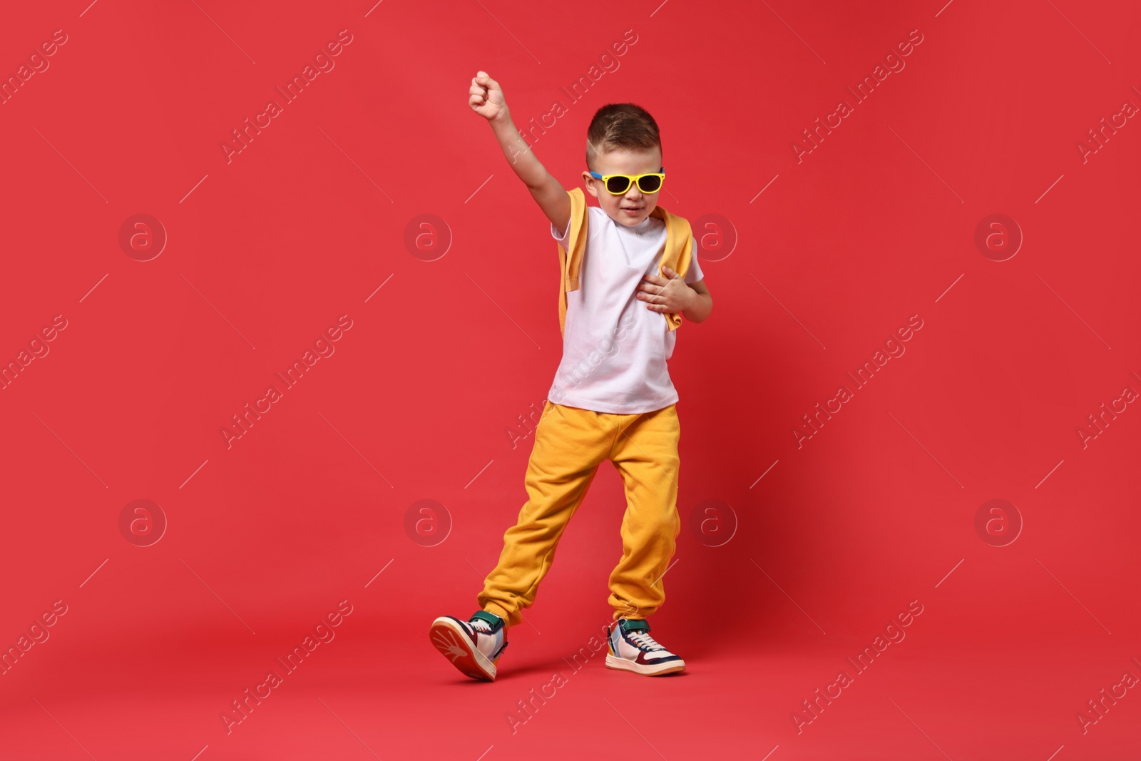 Photo of Happy little boy dancing on red background