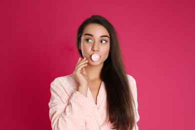Photo of Young woman in bathrobe blowing chewing gum on crimson background