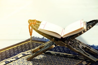 Photo of Rehal with open Quran and Misbaha on Muslim prayer rug indoors