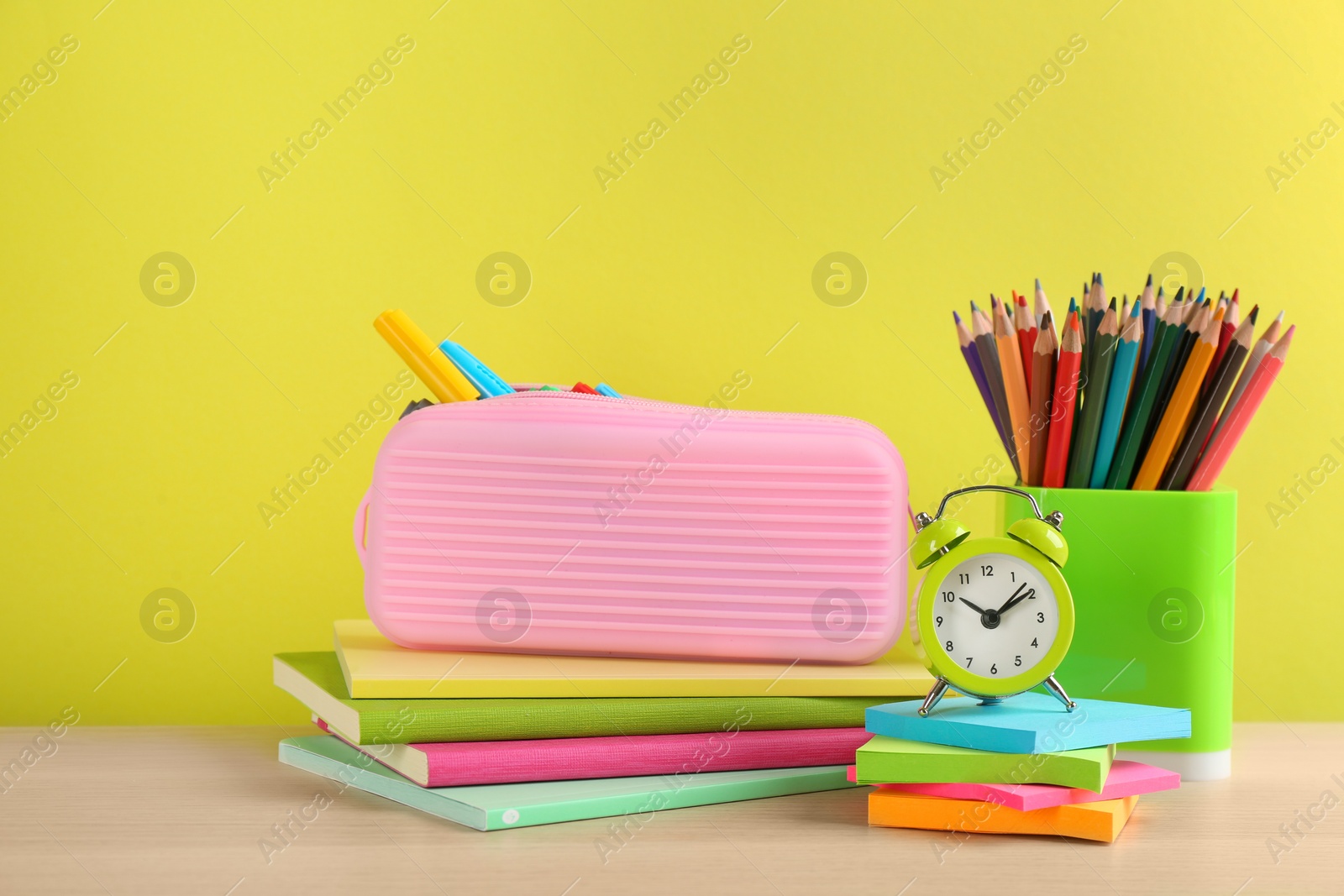 Photo of Different school stationery and alarm clock on table against yellow background. Back to school