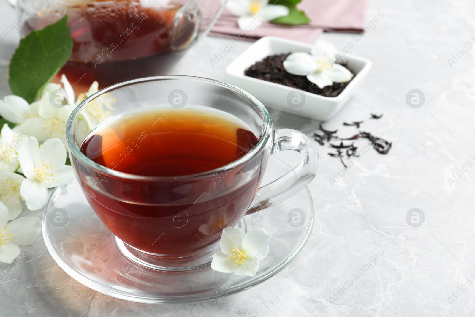 Photo of Cup of tea and fresh jasmine flowers on light grey marble table