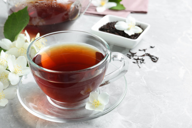 Photo of Cup of tea and fresh jasmine flowers on light grey marble table