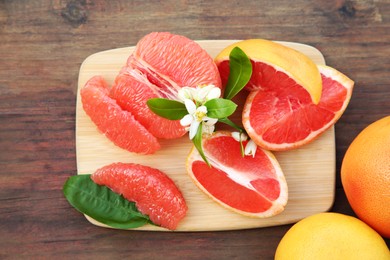 Photo of Fresh ripe grapefruits and green leaves on wooden table, flat lay