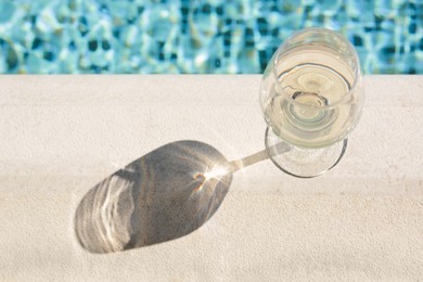 Photo of Glass of tasty wine on swimming pool edge, above view. Space for text