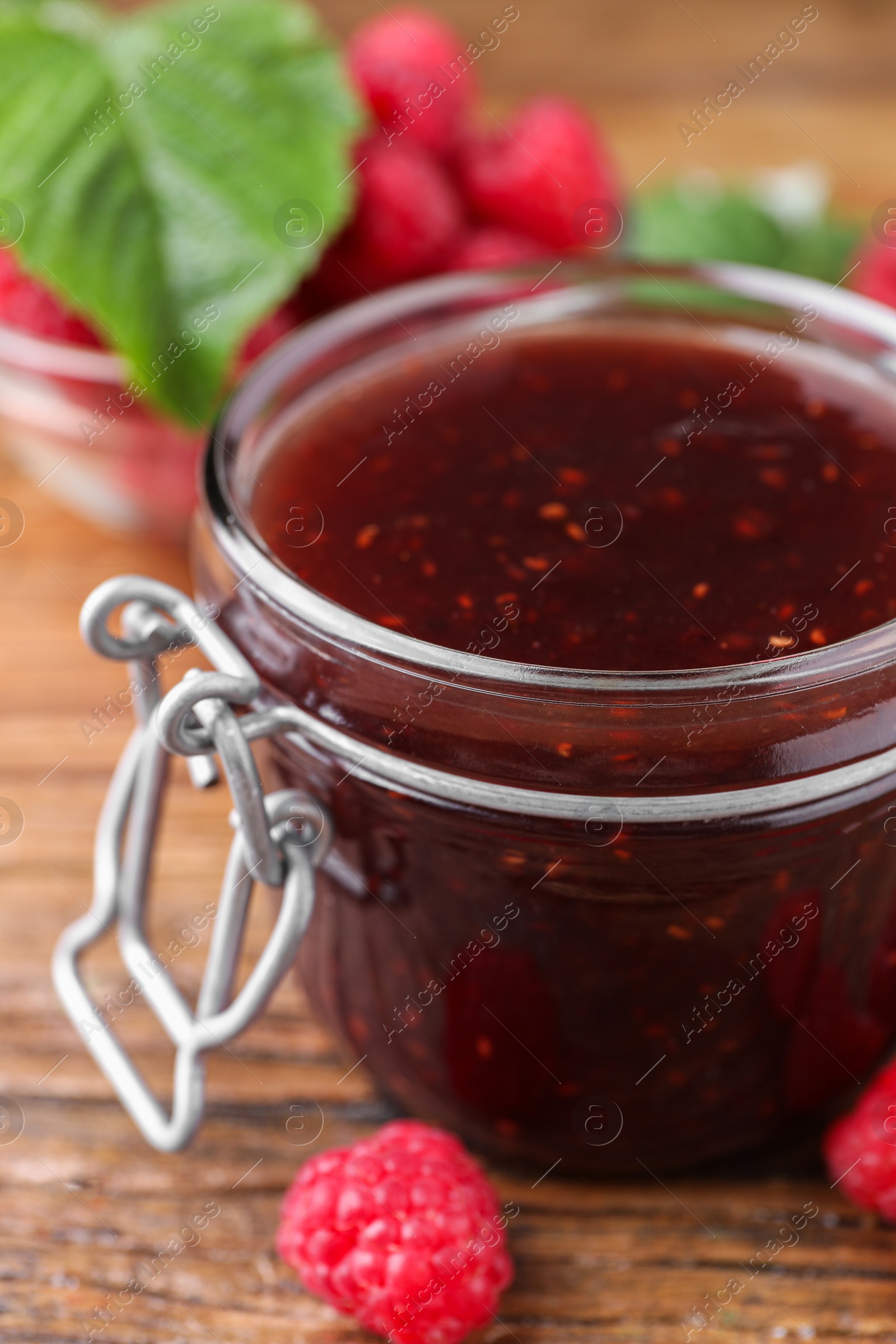 Photo of Jar of delicious raspberry jam and fresh berries on wooden table, closeup