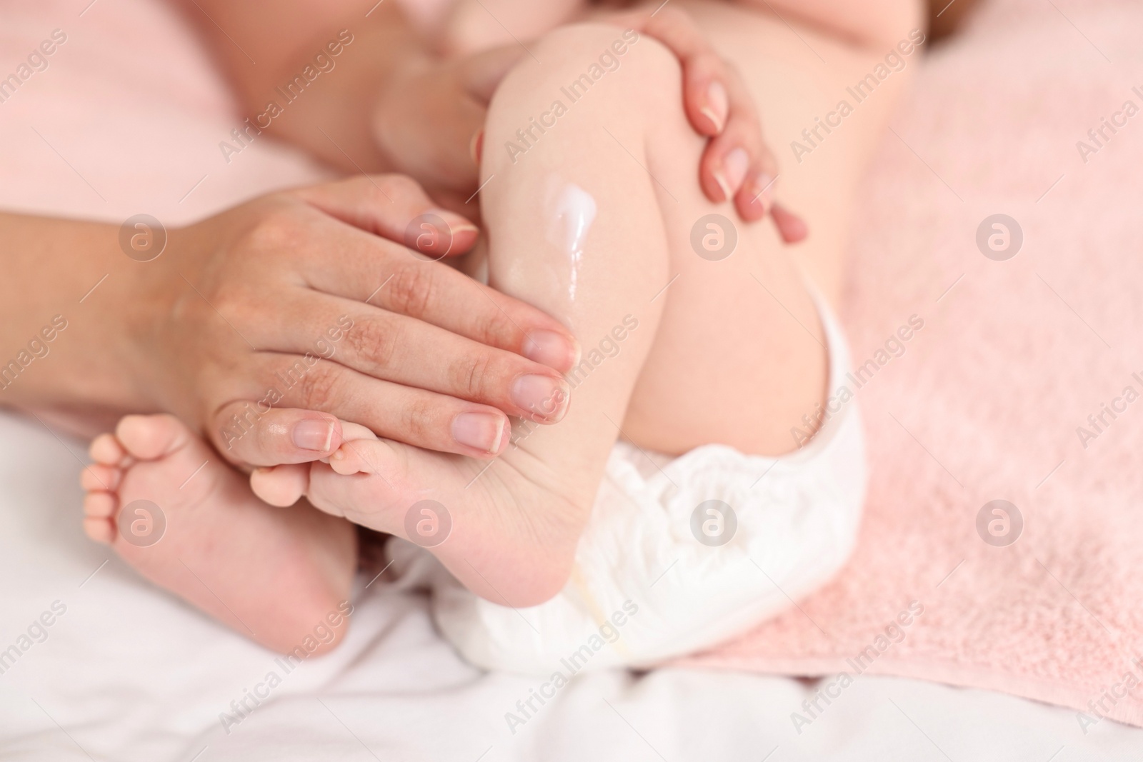 Photo of Woman applying body cream onto baby`s skin on bed, closeup