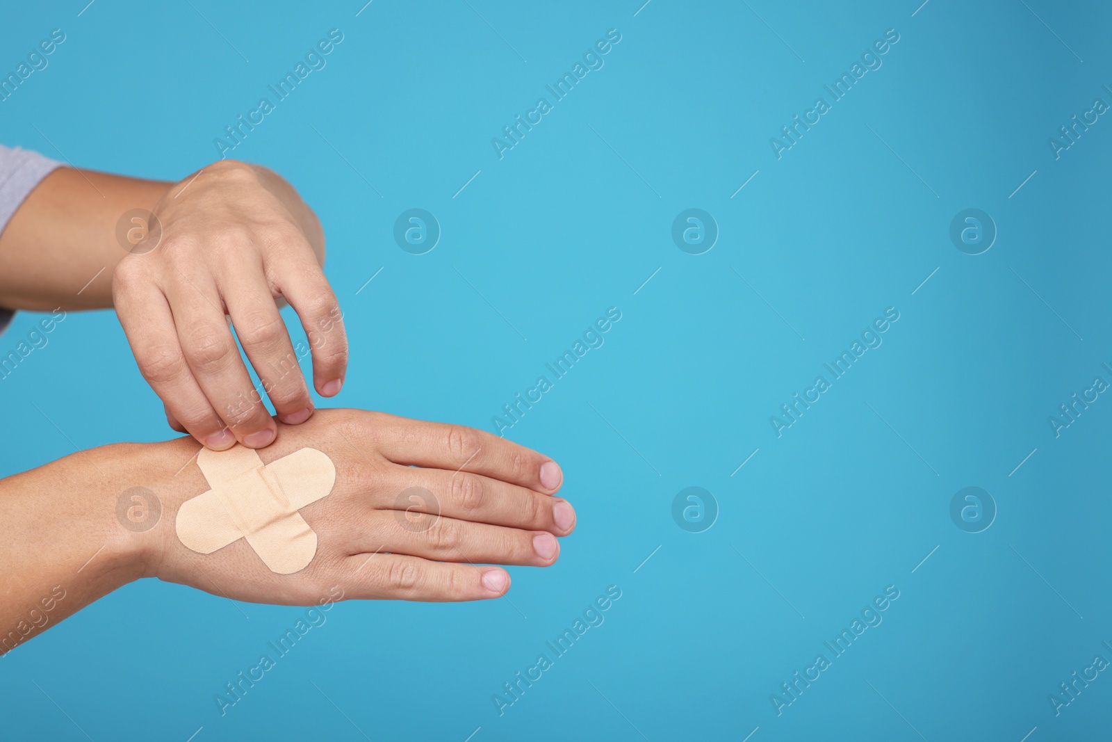 Photo of Man putting sticking plasters onto hand on light blue background, closeup. Space for text