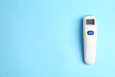 Photo of Modern non-contact infrared thermometer on light blue background, top view. Space for text