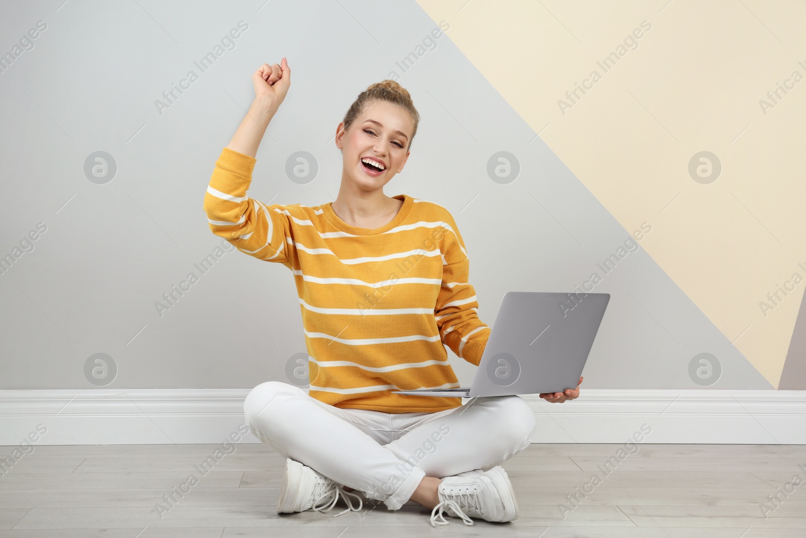 Photo of Emotional young woman with laptop on floor near color wall