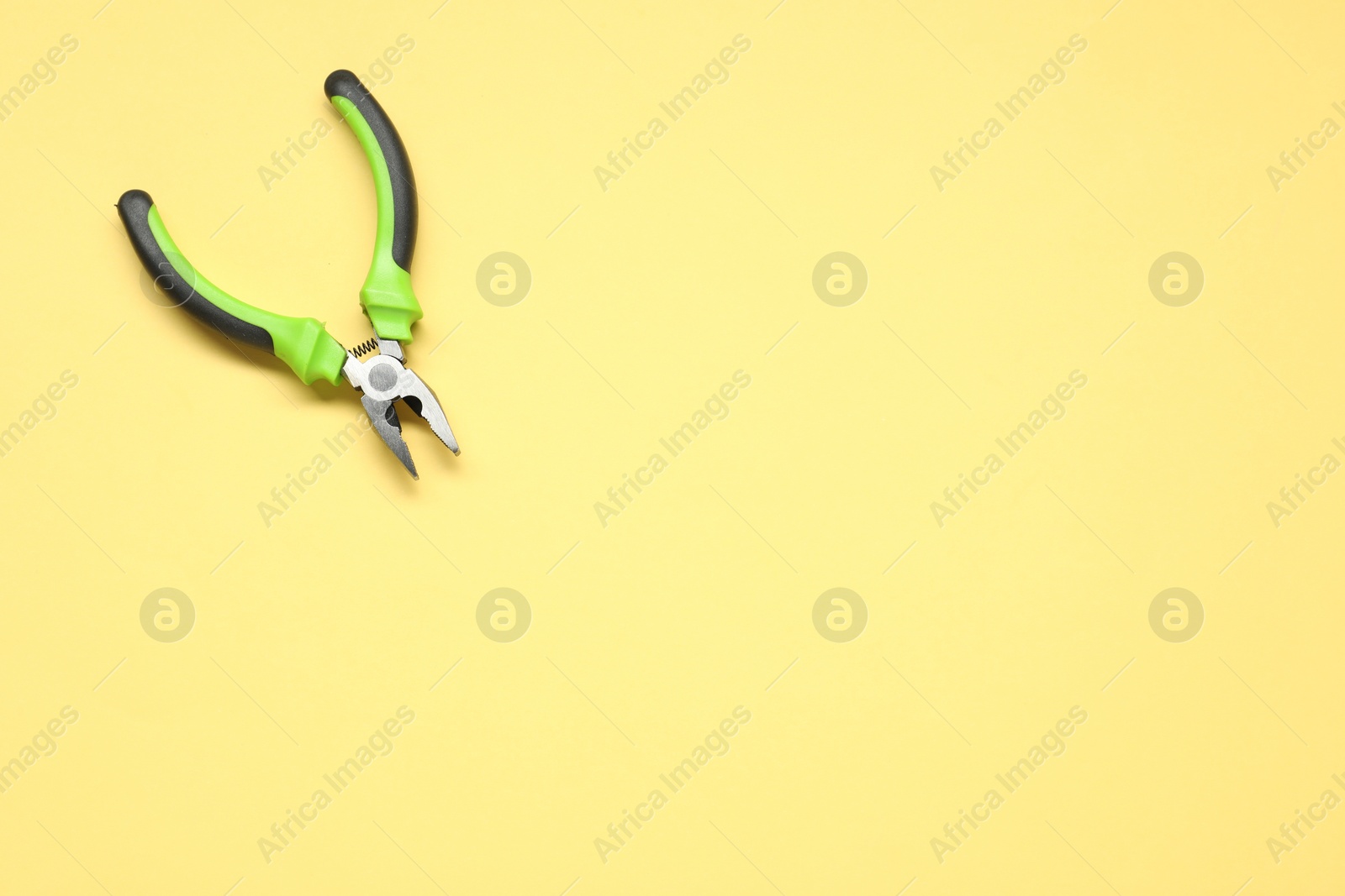 Photo of Combination pliers on yellow background, top view. Space for text