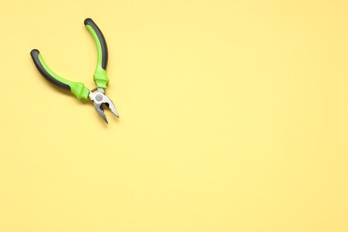 Combination pliers on yellow background, top view. Space for text