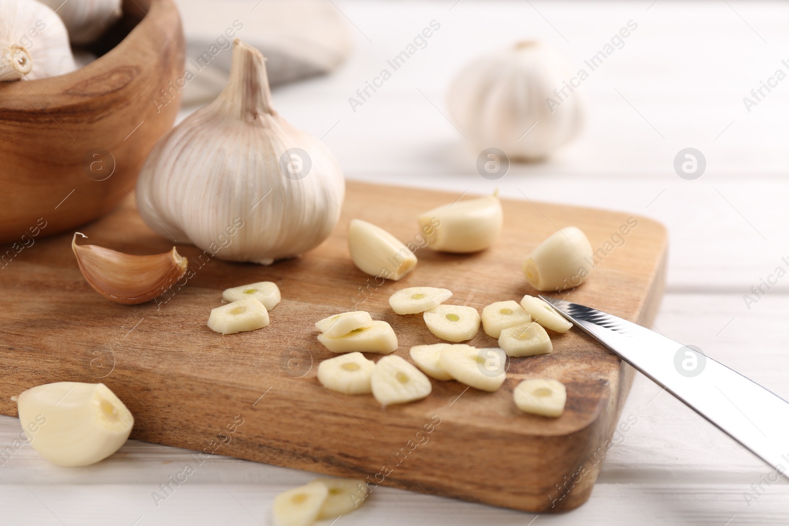 Photo of Aromatic cut garlic, cloves and bulbs on white wooden table, closeup