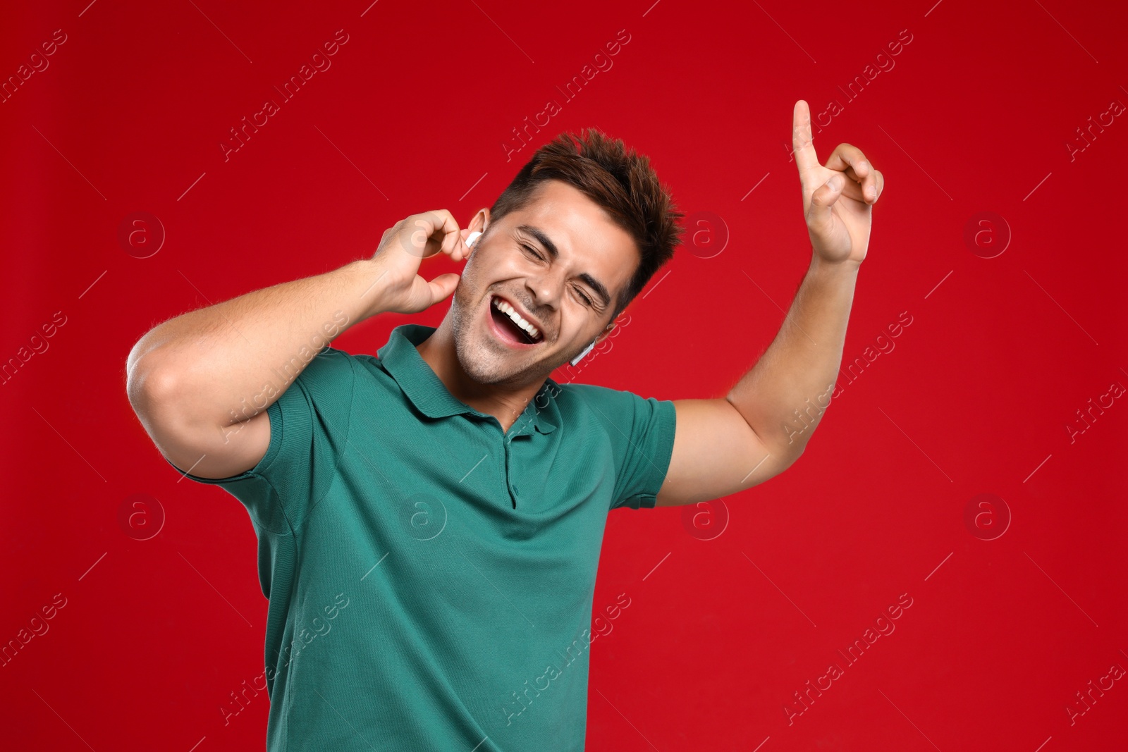 Photo of Happy young man listening to music through wireless earphones on red background