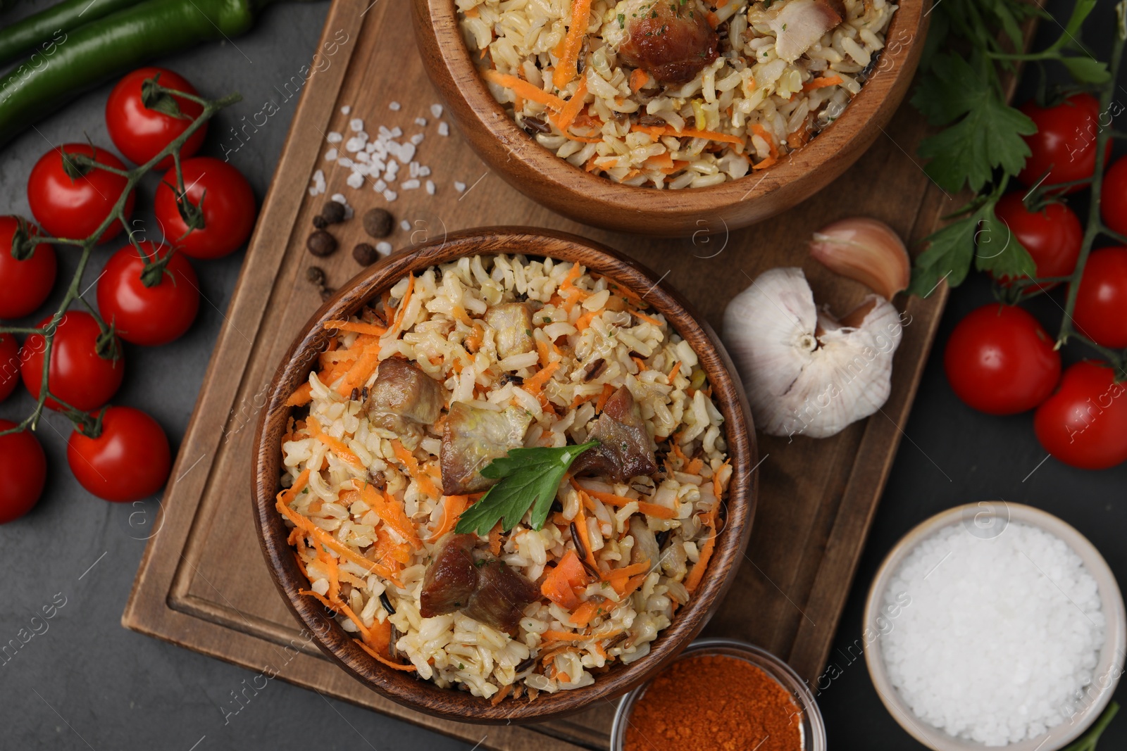 Photo of Delicious pilaf in bowls and products on black table, flat lay