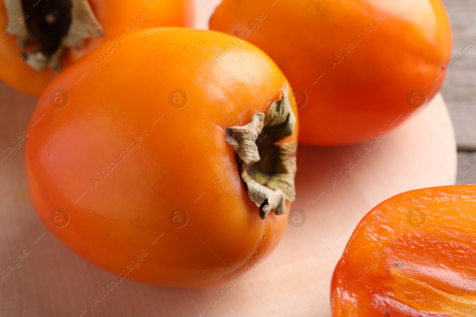 Photo of Whole and cut delicious ripe persimmons on wooden table, closeup