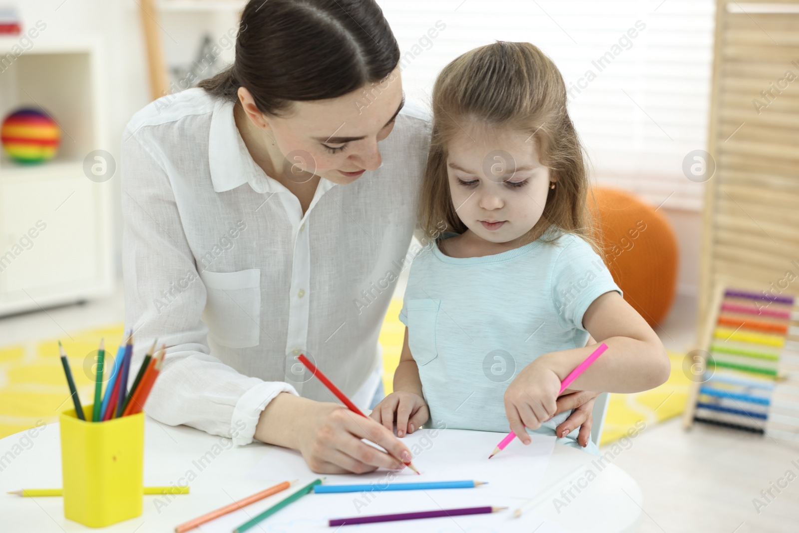 Photo of Mother and her little daughter drawing with colorful pencils at home