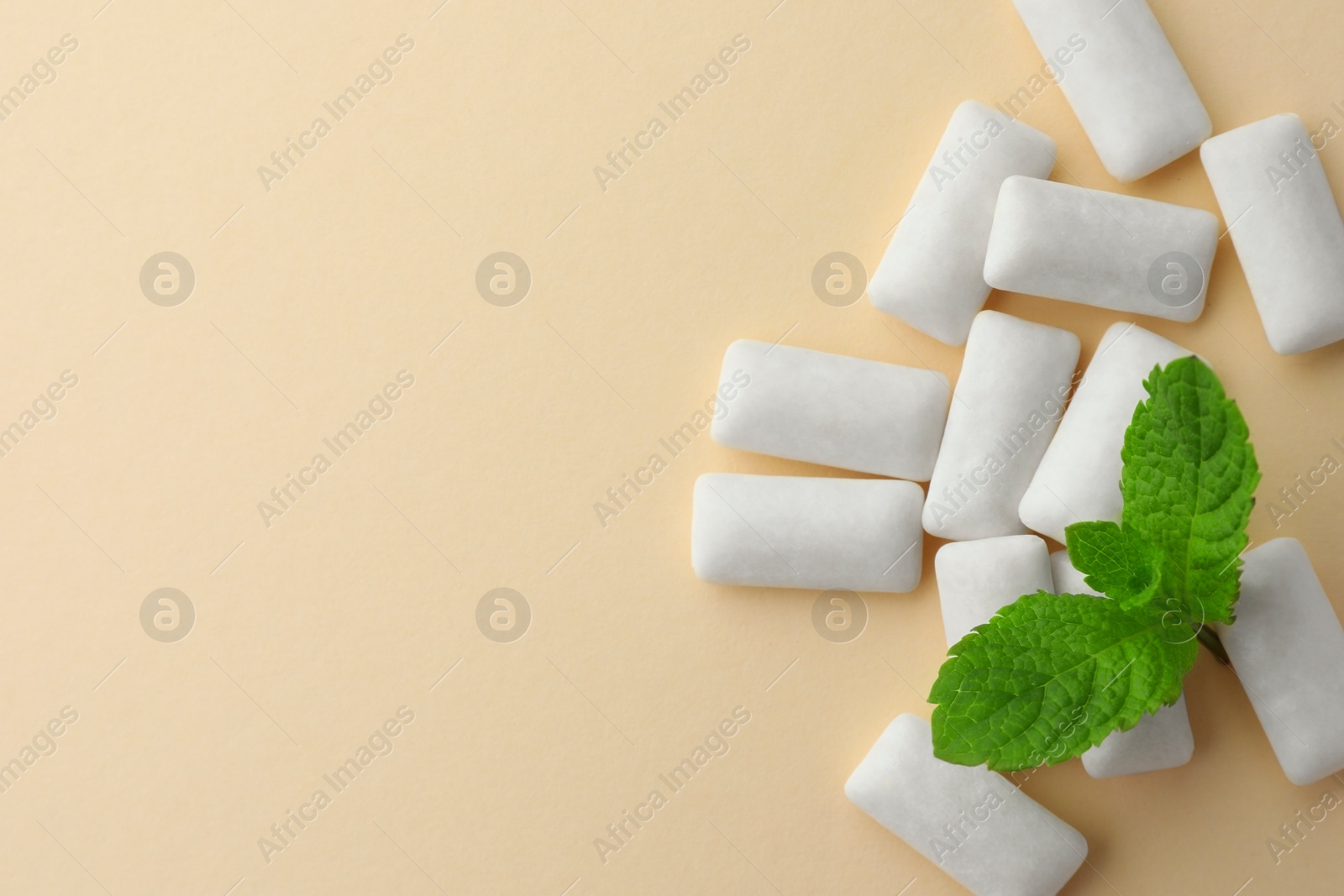 Photo of Tasty white chewing gums and mint leaves on beige background, flat lay. Space for text