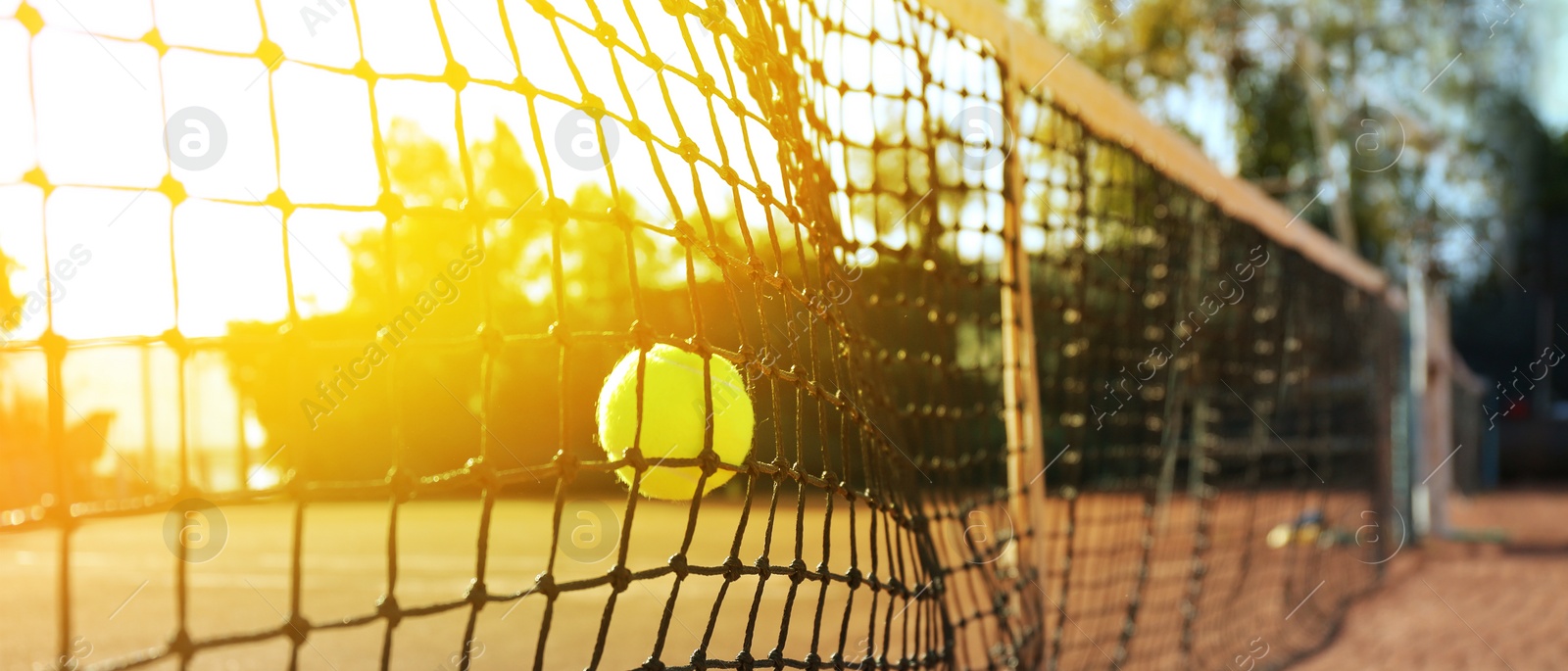 Image of Bright yellow tennis ball hitting into net outdoors on sunny day, banner design