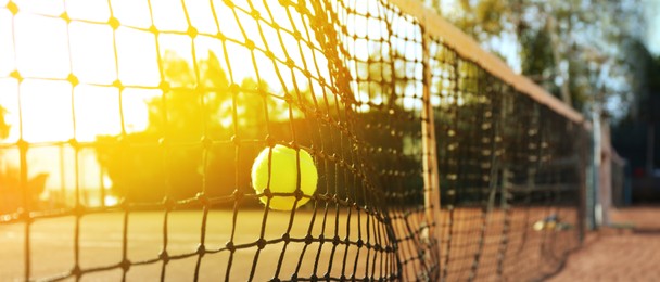 Bright yellow tennis ball hitting into net outdoors on sunny day, banner design