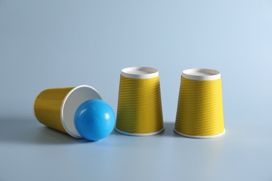 Photo of Shell game. Three yellow cups and ball on light blue background