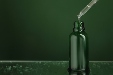 Photo of Dripping face serum into bottle on wet surface against green background, closeup. Space for text