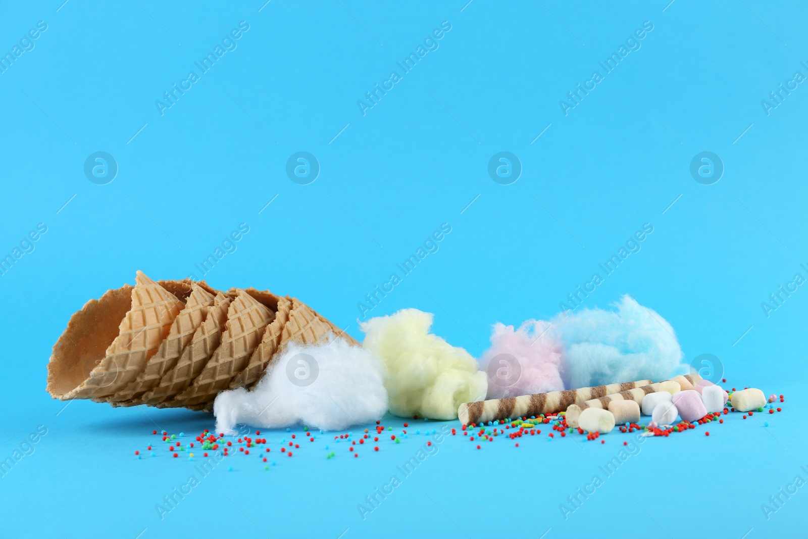 Photo of Sweet cotton candies, waffle cones, wafer sticks and marshmallows on light blue background