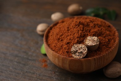 Nutmeg powder and halves of seed in bowl on wooden table, closeup. Space for text