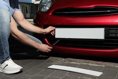 Photo of Man changing vehicle registration plate on car outdoors, closeup