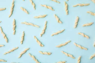 Uncooked trofie pasta on light blue background, flat lay