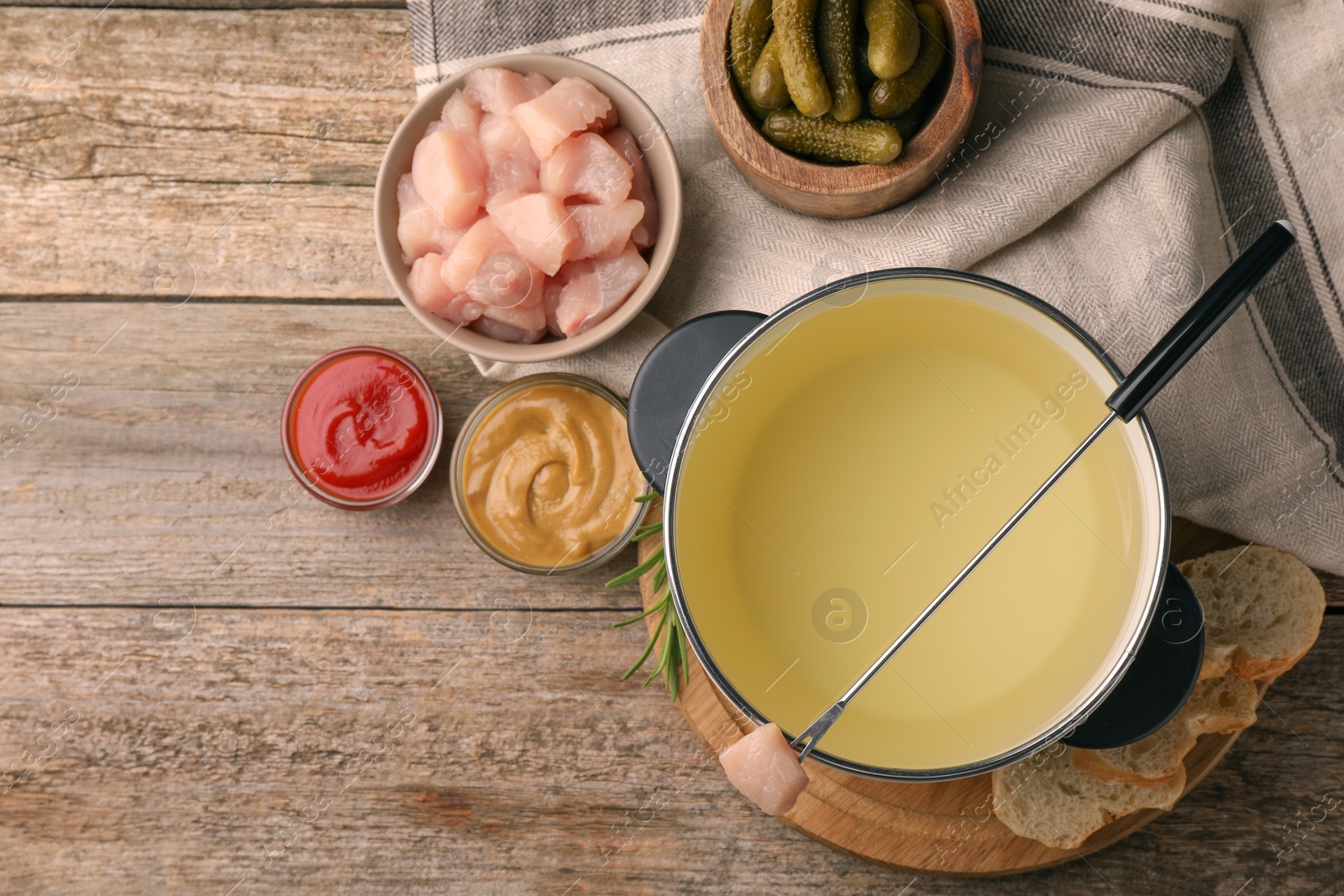 Photo of Fondue pot with oil, fork, raw meat pieces and other products on wooden table, flat lay. Space for text