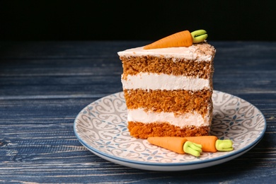 Photo of Piece of sweet carrot cake with delicious cream on blue wooden table against dark background. Space for text