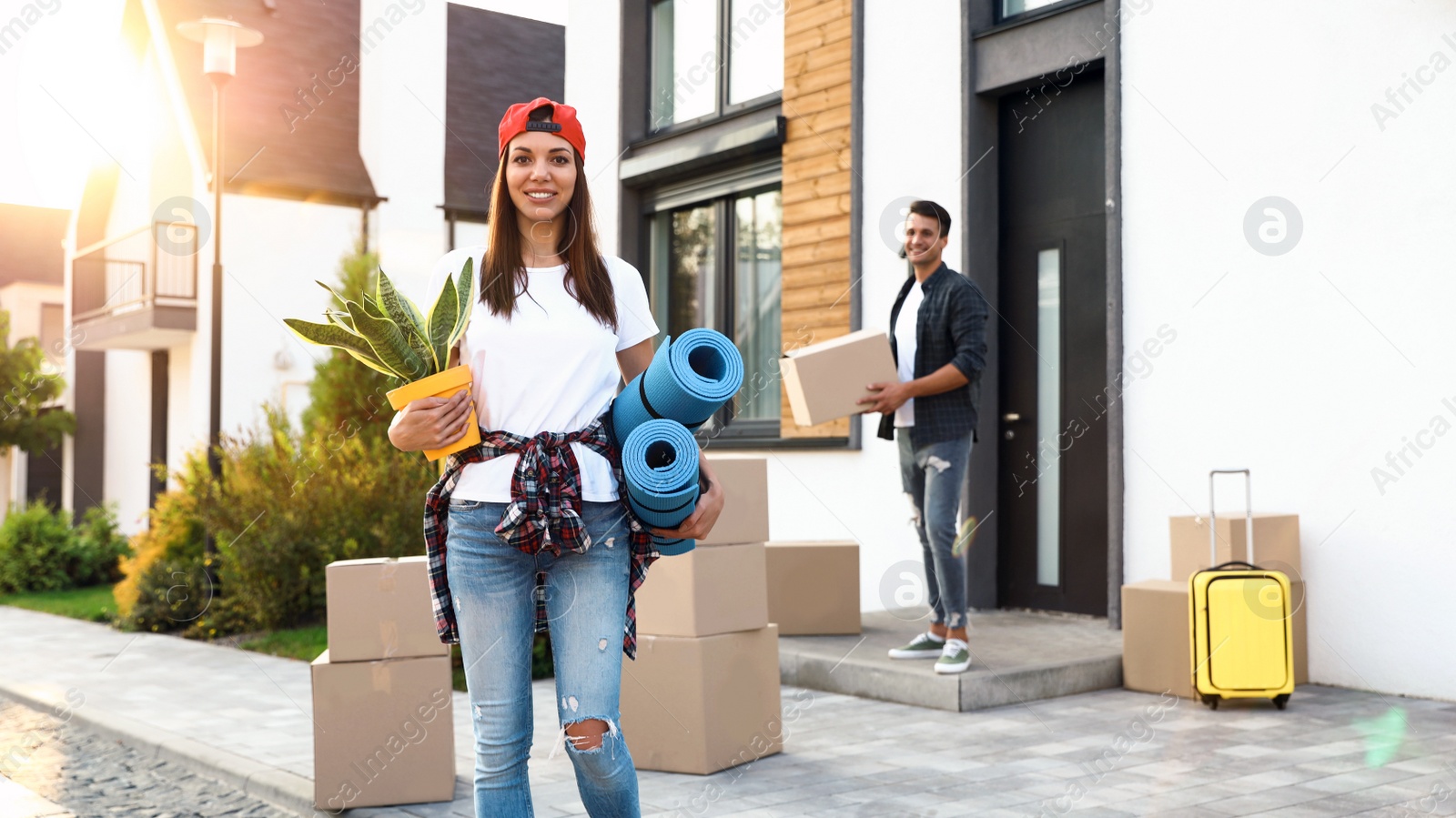 Photo of Happy couple with moving boxes and household stuff near their new house on sunny day