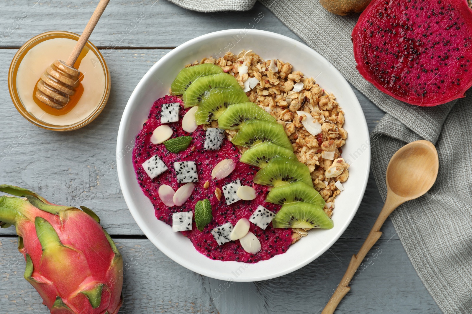 Photo of Bowl of granola with pitahaya, kiwi and almonds served on grey wooden table, flat lay