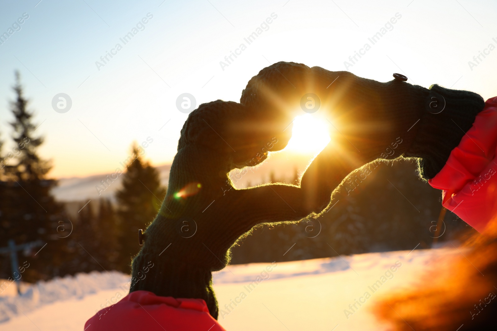 Photo of Woman making heart with hands outdoors at sunset, closeup. Winter vacation