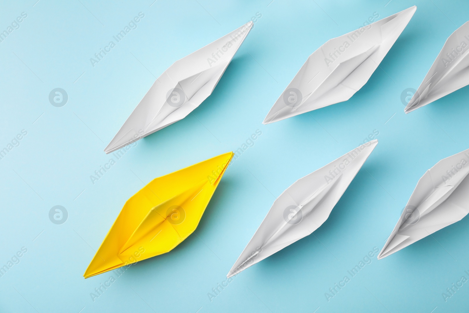 Photo of Group of paper boats following yellow one on light blue background, flat lay. Leadership concept