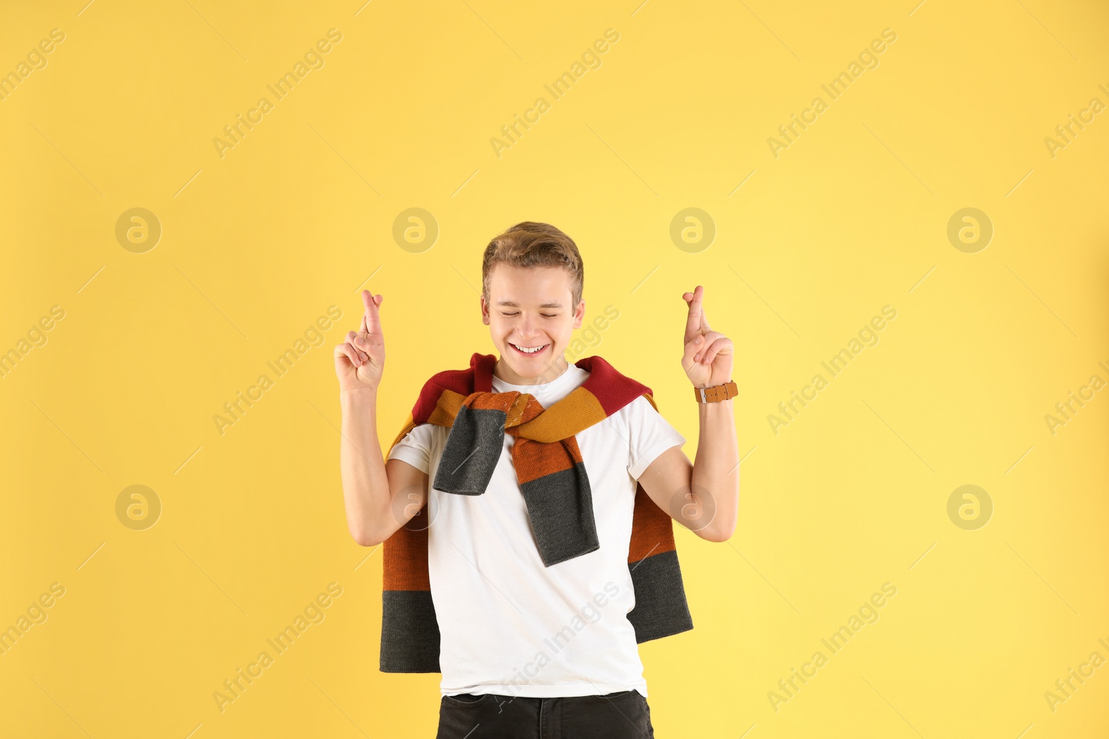 Photo of Emotional teenage boy crossing his fingers on color background