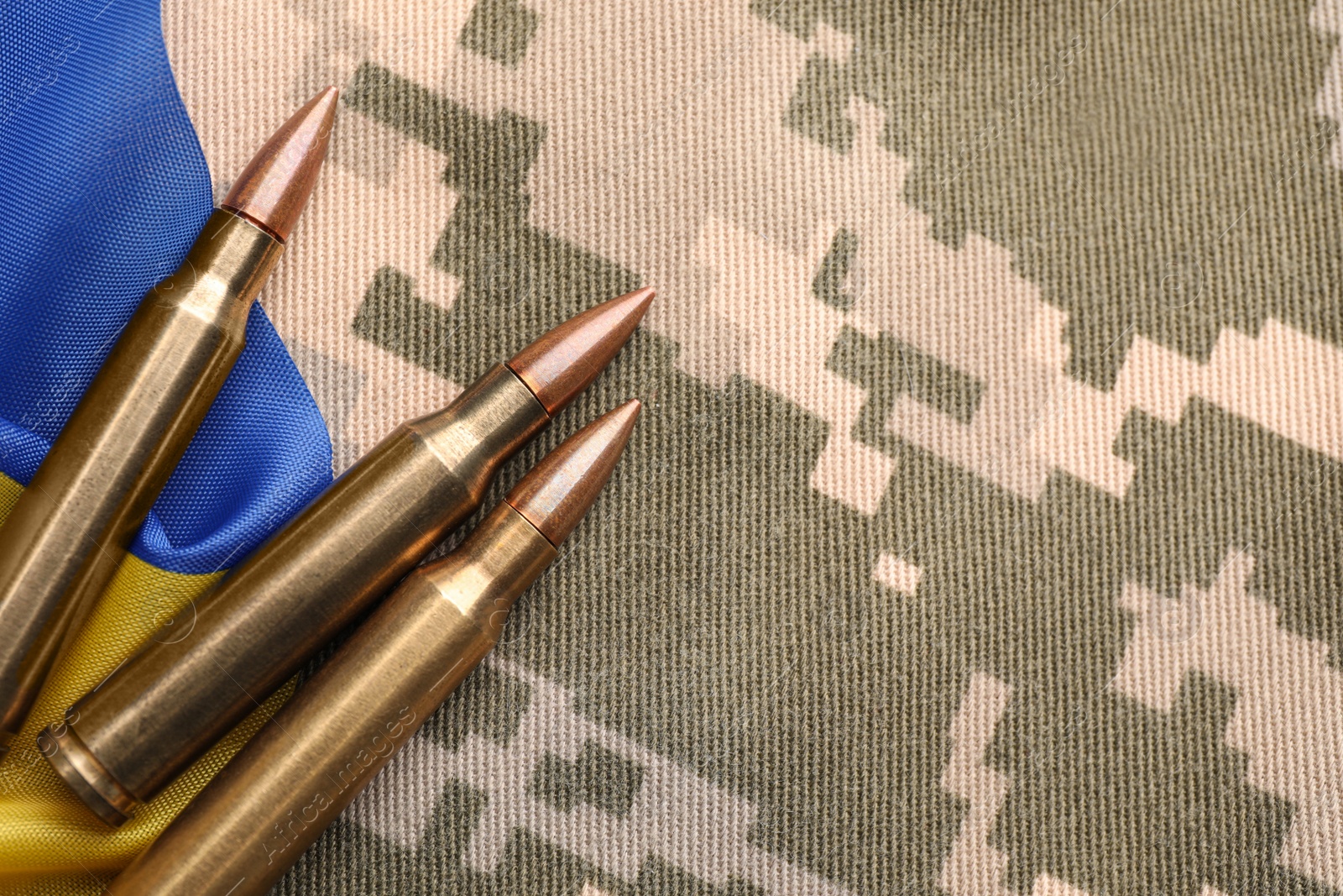 Photo of Military bullets and Ukrainian flag on pixel camouflage, flat lay. Space for text