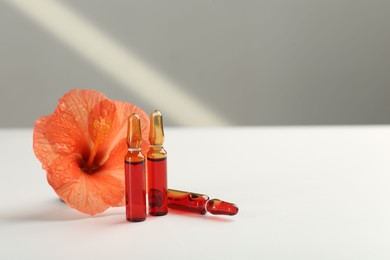 Skincare ampoules and hibiscus flower on white table. Space for text