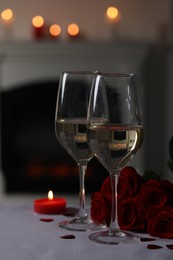 Photo of Glasses of white wine, burning candle and rose flowers on grey table against blurred lights. Romantic atmosphere