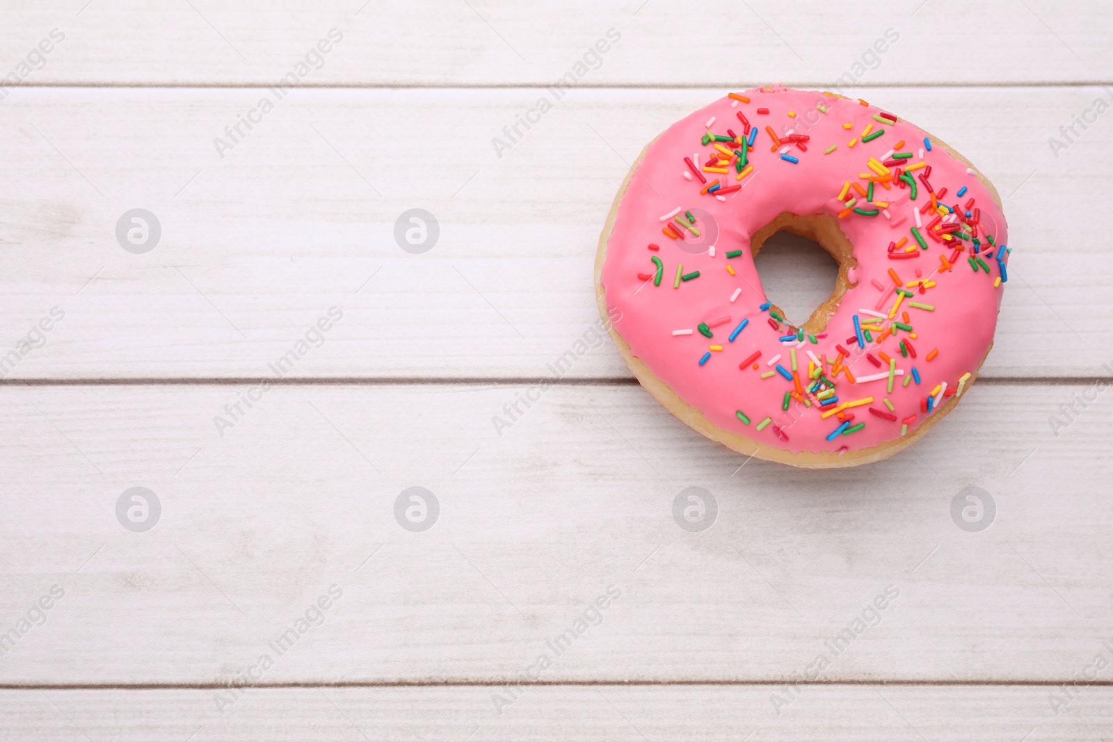 Photo of Glazed donut decorated with sprinkles on white wooden table, top view. Space for text. Tasty confectionery