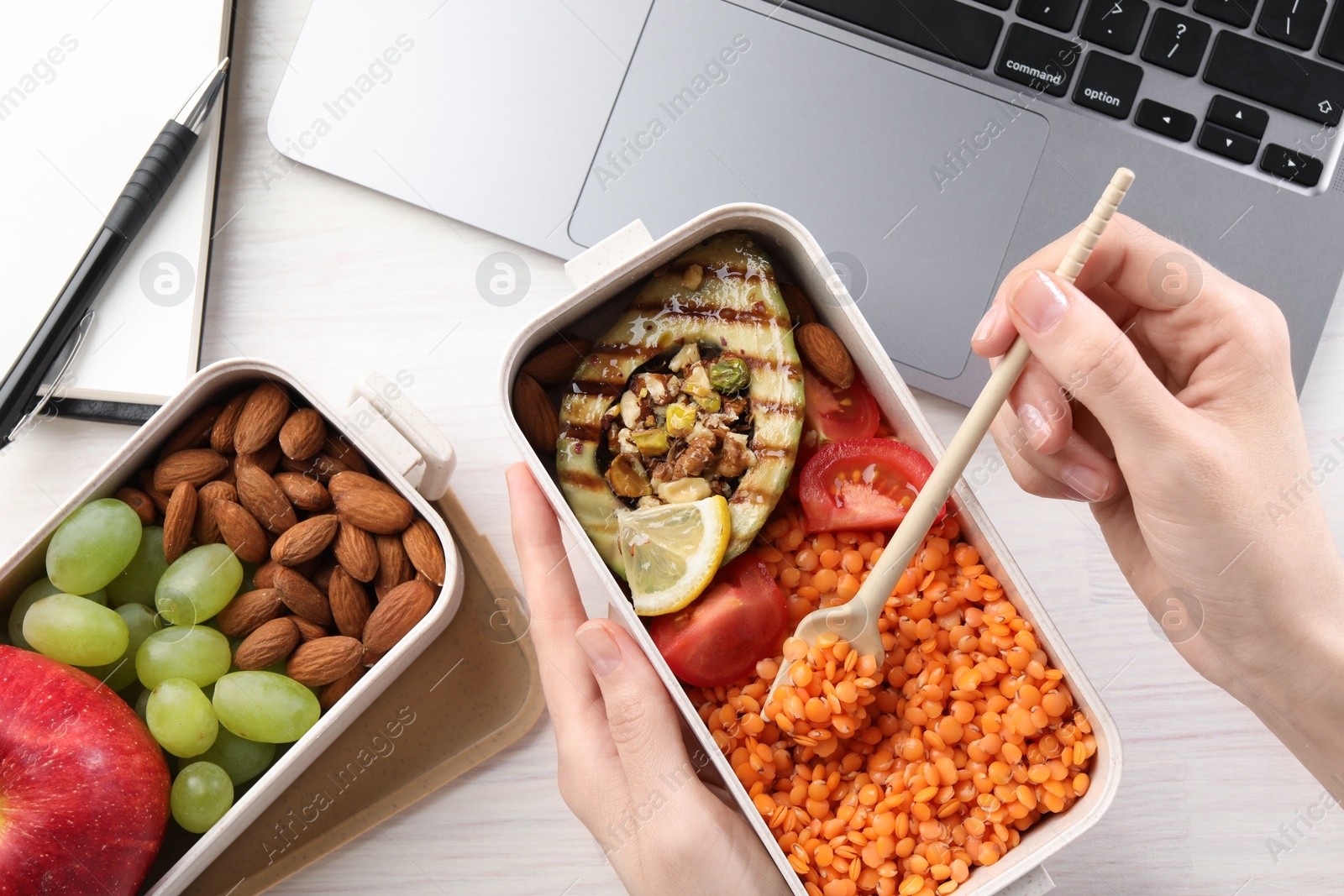 Photo of Woman eating healthy products high in vegetable fats near laptop at light wooden table, top view