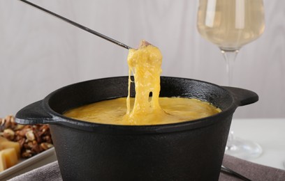 Dipping piece of ham into fondue pot with tasty melted cheese, closeup