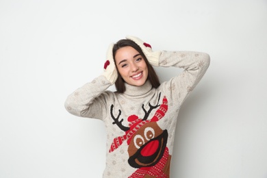 Young woman in Christmas sweater and mittens on white background