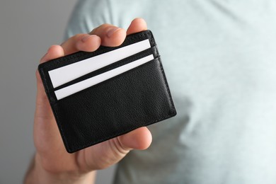 Man holding leather business card holder with cards on grey background, closeup