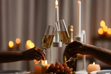 Photo of Couple clinking glasses of champagne against burning candles, closeup