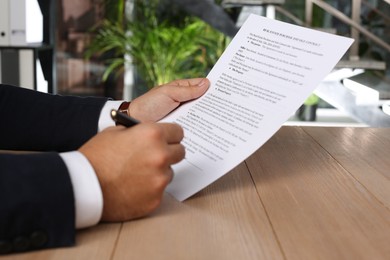 Photo of Man signing Real Estate Purchase And Sale Contract at wooden table indoors, closeup