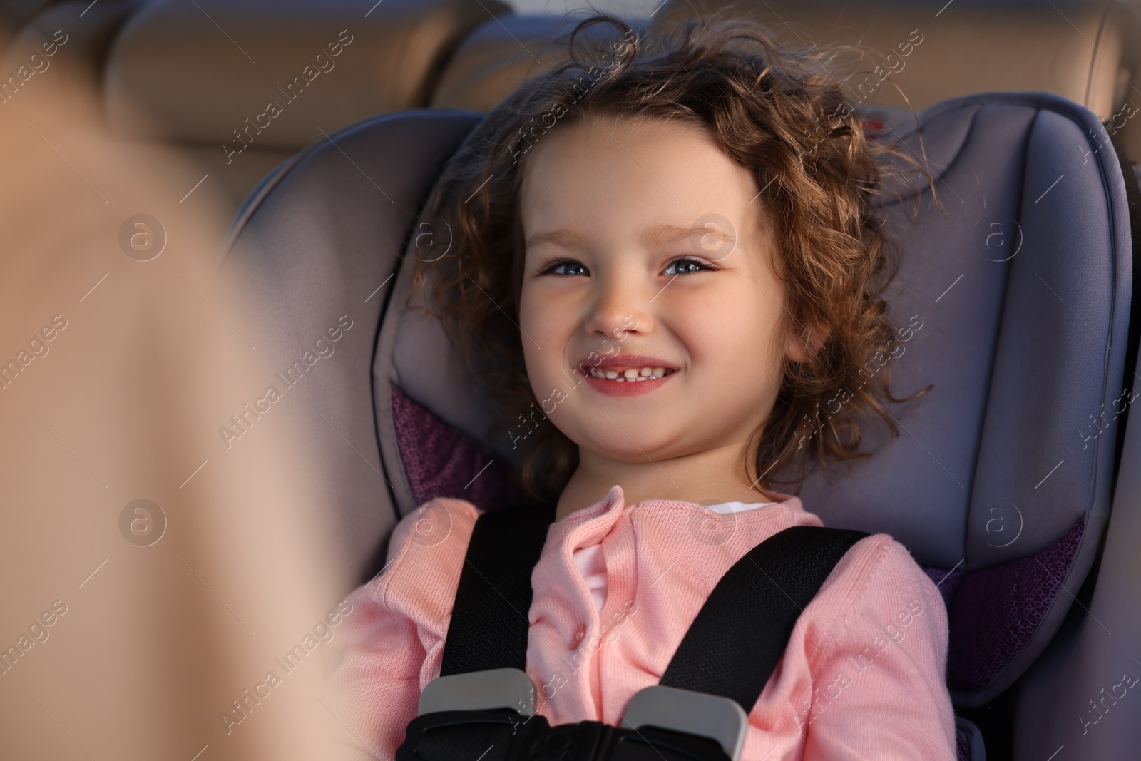 Photo of Cute little girl sitting in child safety seat inside car