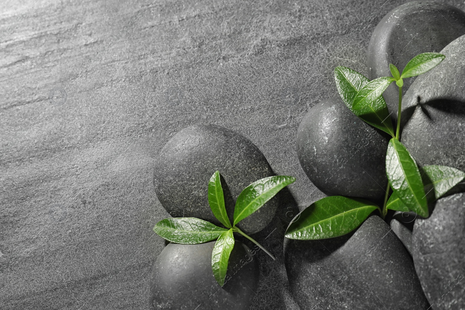 Photo of Spa stones and green leaves on grey table, flat lay with space for text